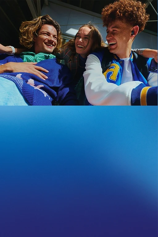  Drei junge Menschen sitzen nah beieinander. Eine Person hält ein Smartphone. Alle lächeln. 